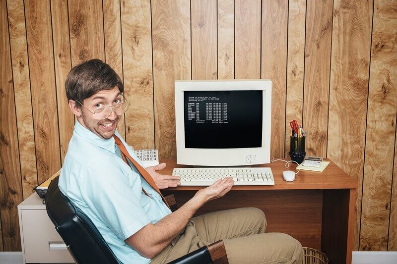 Man looking at you and pointing his hands at an old computer
